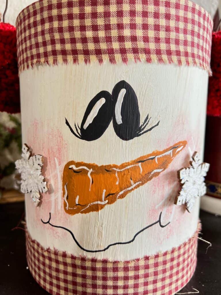 Close up of the hand painted snowman face on the coffee can with snowflakes for cheeks.