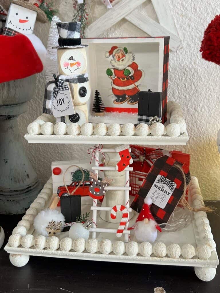Small 2 tiered white tiered tray all decorated for Christmas with the wood block snowman on the top tier.