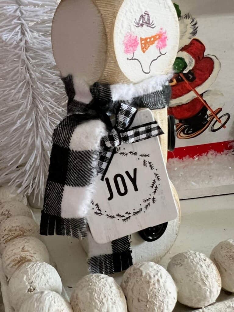 The snowman with a buffalo check scarf and a small white and black hangtag that says "joy".