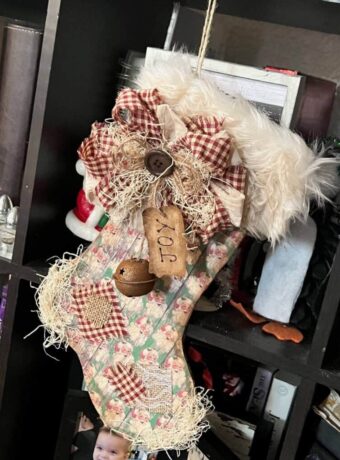 DIY Christmas Stocking made from cardboard with vintage red and green santa scrapbook paper, burlap patches, a messy fabric bow, a "joy" hangtag, a rusty bell, and grungy faux fur hanging with twine.