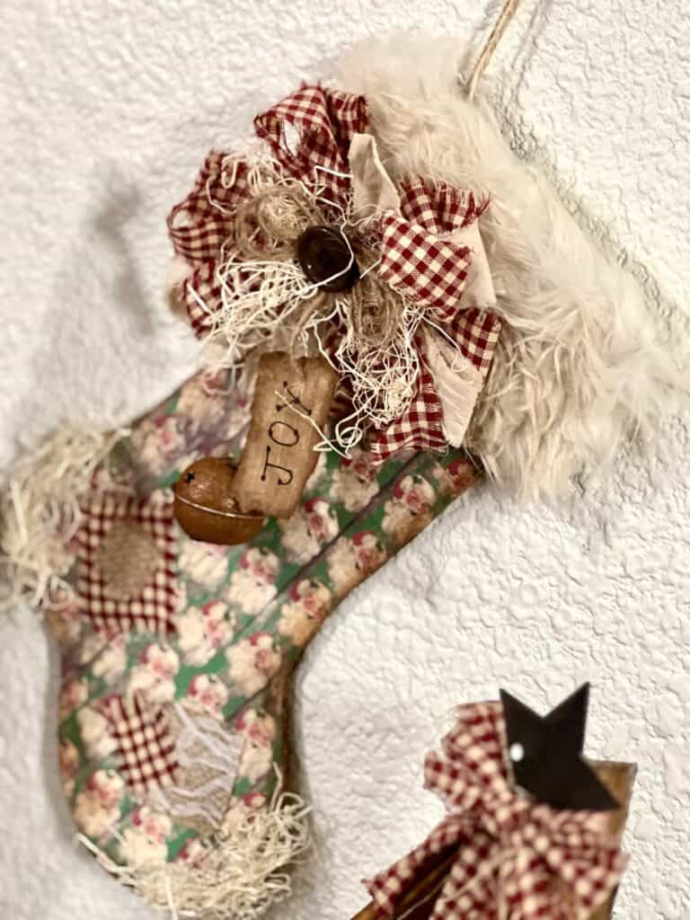 DIY Christmas Stocking made from cardboard with vintage red and green santa scrapbook paper, burlap patches, a messy fabric bow, a "joy" hangtag, a rusty bell, and grungy faux fur hanging with twine.