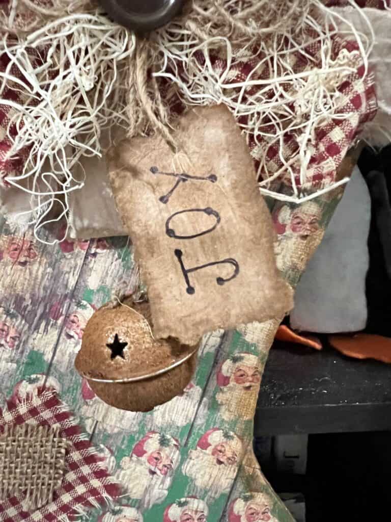 A hangtag that says "Joy" made from kraft paper and a rusty bell hanging from the bow on the top of the stocking.