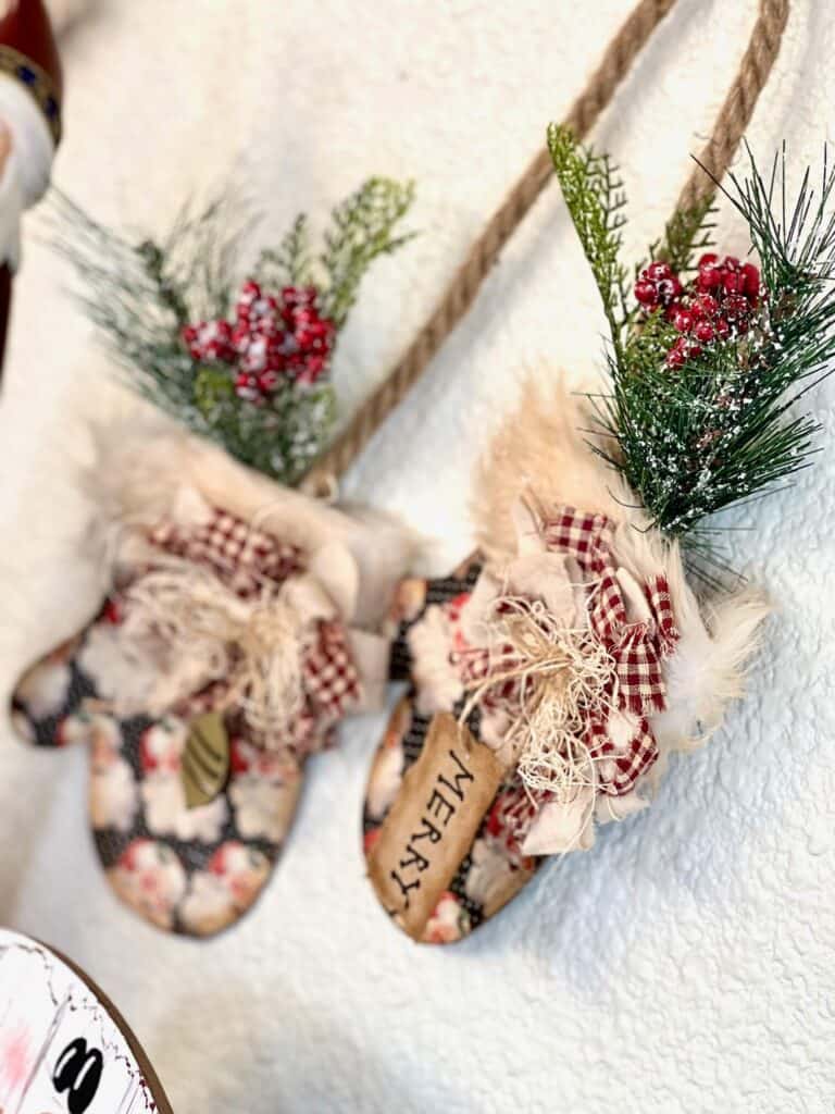 Close up of the DIY christmas mittens of the mitten on the right with the greenery and berries coming out the top of the fur cuff and a small bow with a hangtag that says "merry".