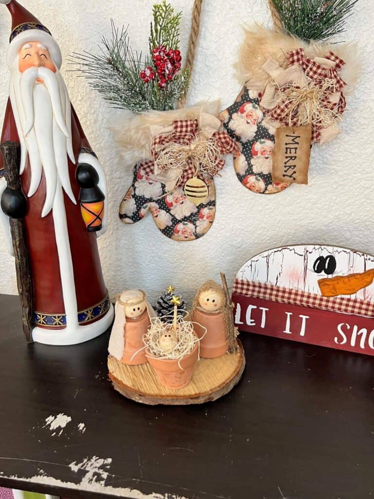 The simple rustic nativity set sitting on a bookshelf with a snowman and a santa next to it.
