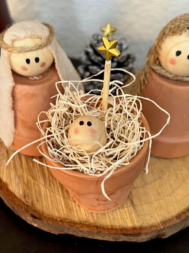 Mini terra cotta pot baby jesus in his manger with a wood bead head and a simple hand drawn face.