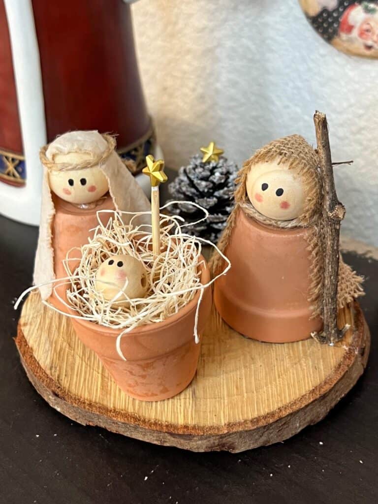 DIY Mini Terra cotta pot nativity set made with a rustic wood round, with mary, joseph, and baby jesus as natural wood beads and a mini pine cone christmas tree with a star at the top.