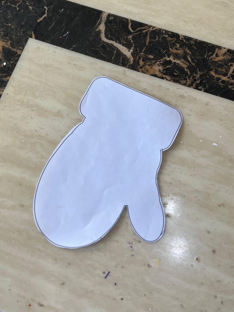 A mitten cut out of copy paper to make a template.