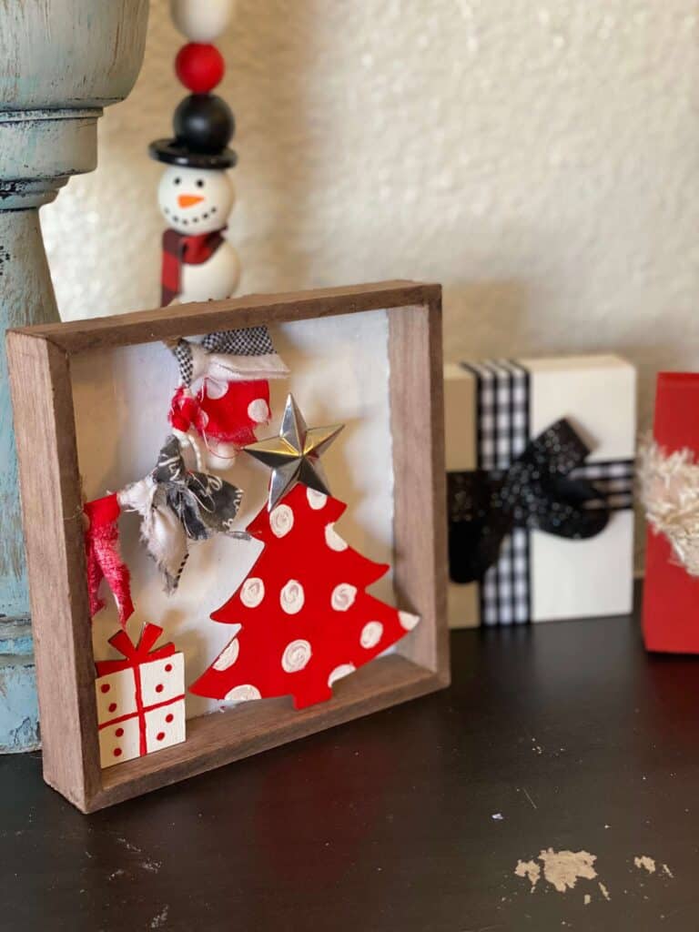 Whimsy Christmas Tree Shelf sitter that is small enough to fit on a tiered tray with a Dollar Tree wood Christmas tree painted red with white polka dots, a small wood present under the tree and a fabric garland in the top left corner. 