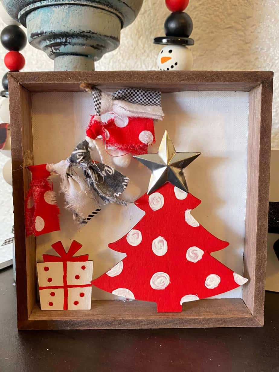 Whimsy Christmas Tree Shelf sitter that is small enough to fit on a tiered tray with a Dollar Tree wood Christmas tree painted red with white polka dots, a small wood present under the tree and a fabric garland in the top left corner.