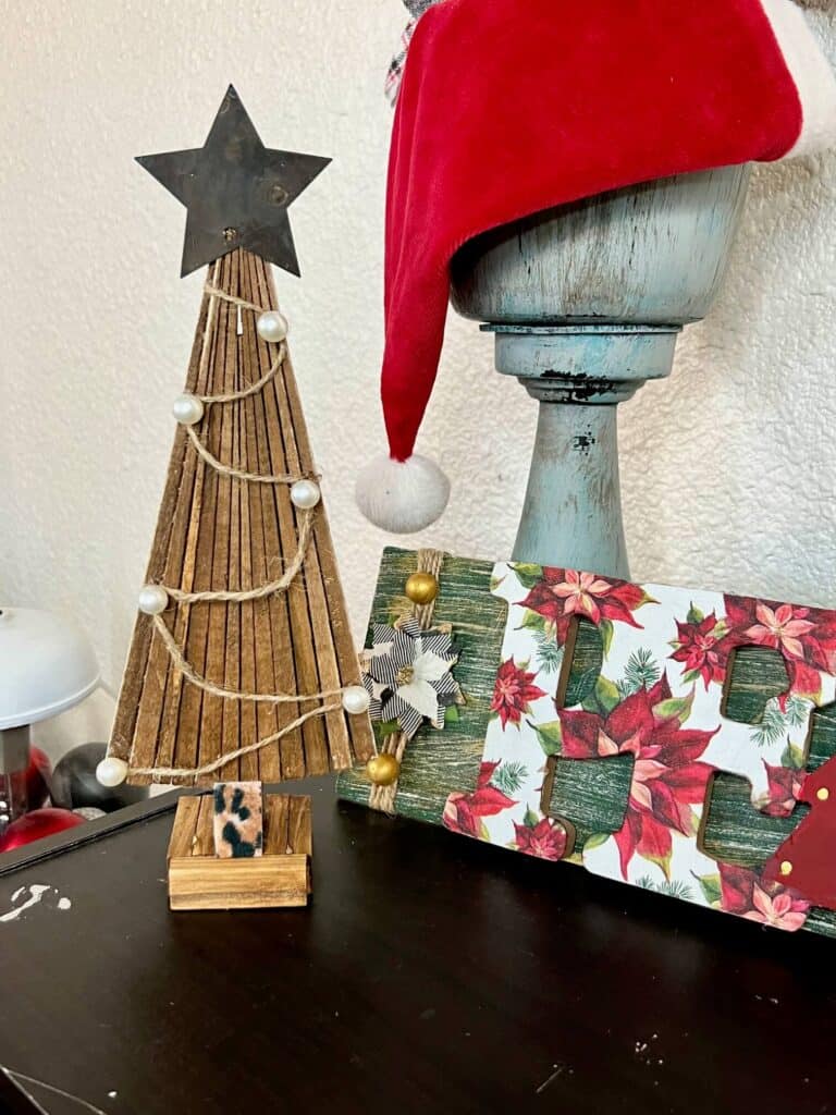 The neutral shim christmas tree next to a chunky candlestick and a Peace Christmas sign on a book