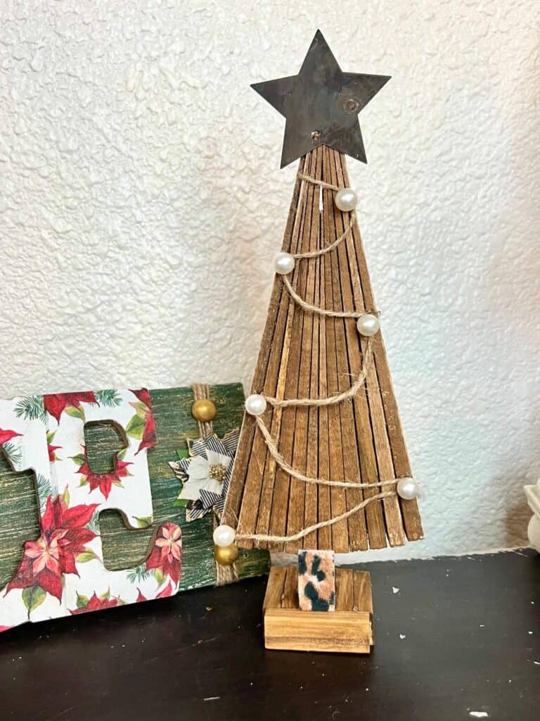 DIY standing Christmas tree decor with wooden shims, music sheet scrapbook paper, twine and pearls ornaments, a metal star and a leopard print trunk and stand made with jenga blocks.