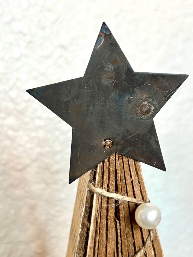 A metal barn star glued to the top of the neutral wood shim christmas tree.
