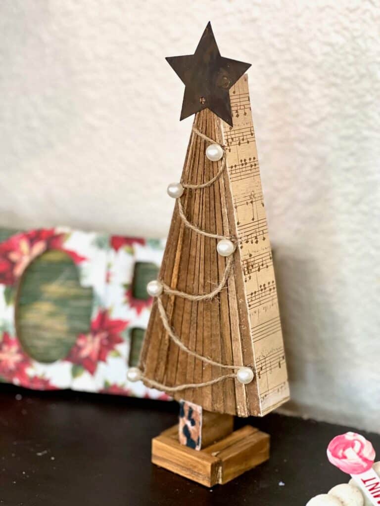 DIY standing Christmas tree decor with wooden shims, music sheet scrapbook paper, twine and pearls ornaments, a metal star and a leopard print trunk and stand made with jenga blocks.
