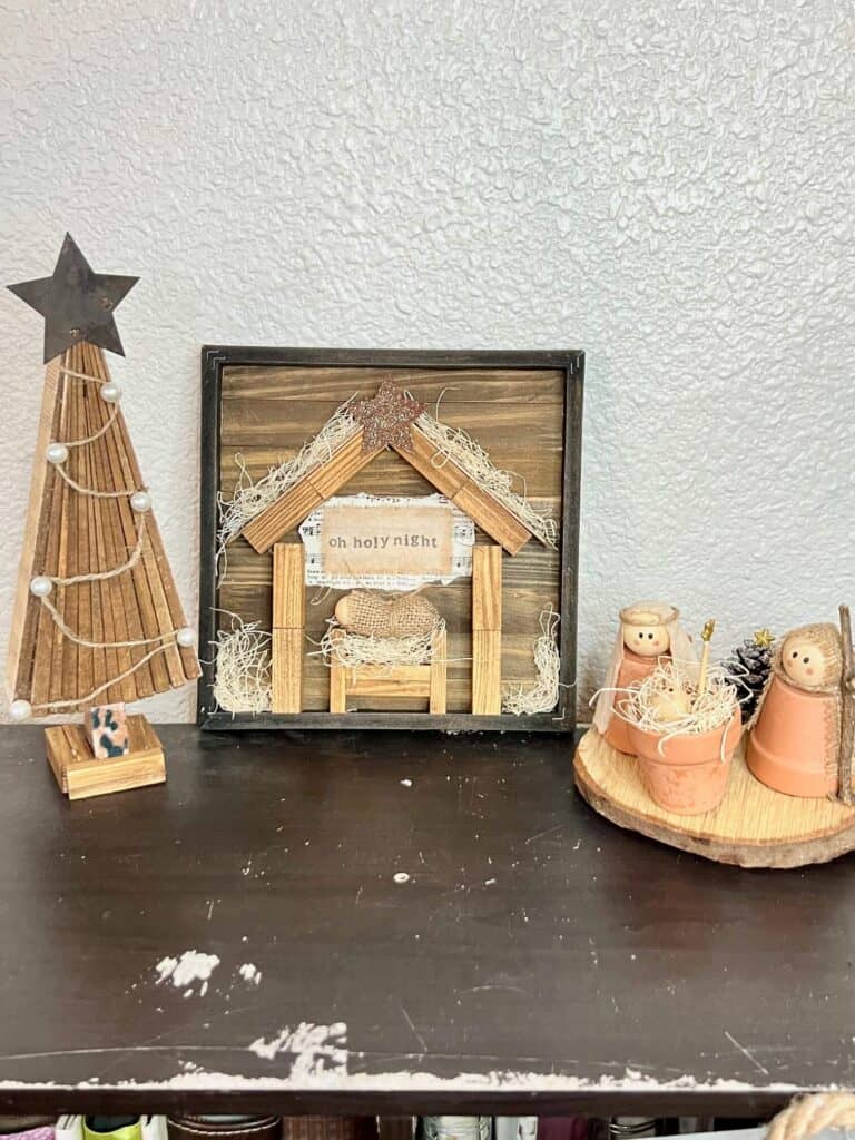 The Shim Christmas Tree on the left, a rustic nativity set in the center and a terra cotta pot nativity set on the right side, all sitting on a bookcase.