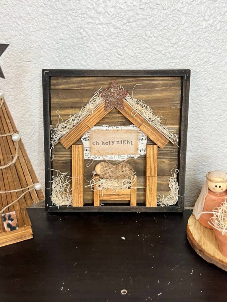 DIY Dollar Tree Rustic Nativity Set made with Jenga Blocks, with a Baby Jesus in a manger with a wood bead and burlap, and the words "oh holy night" stamped on a piece of muslin on top.
