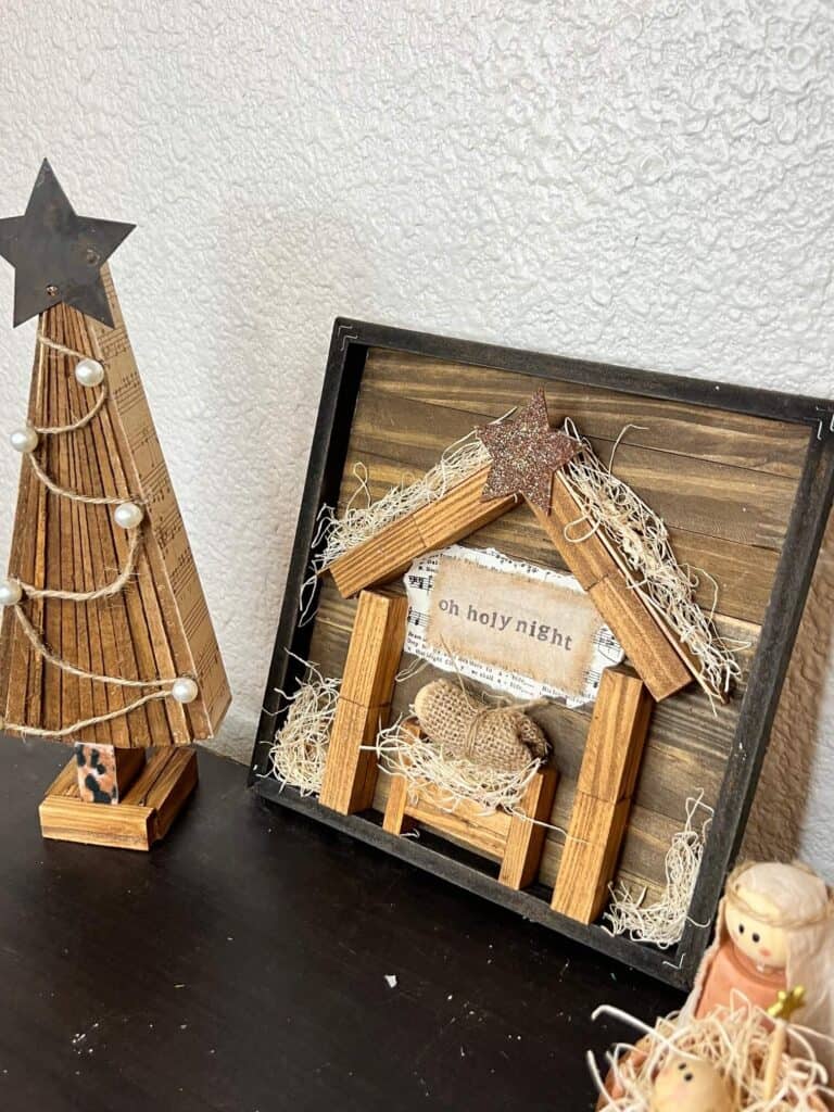The completed Baby Jesus Manger next to a wooden shim christmas tree on a book shelf.