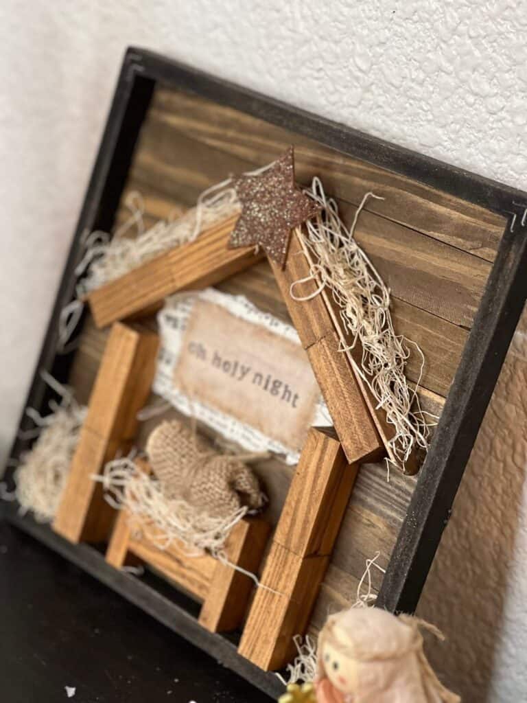 DIY Dollar Tree Rustic Nativity Set made with Jenga Blocks, with a Baby Jesus in a manger with a wood bead and burlap, and the words "oh holy night" stamped on a piece of muslin on top.