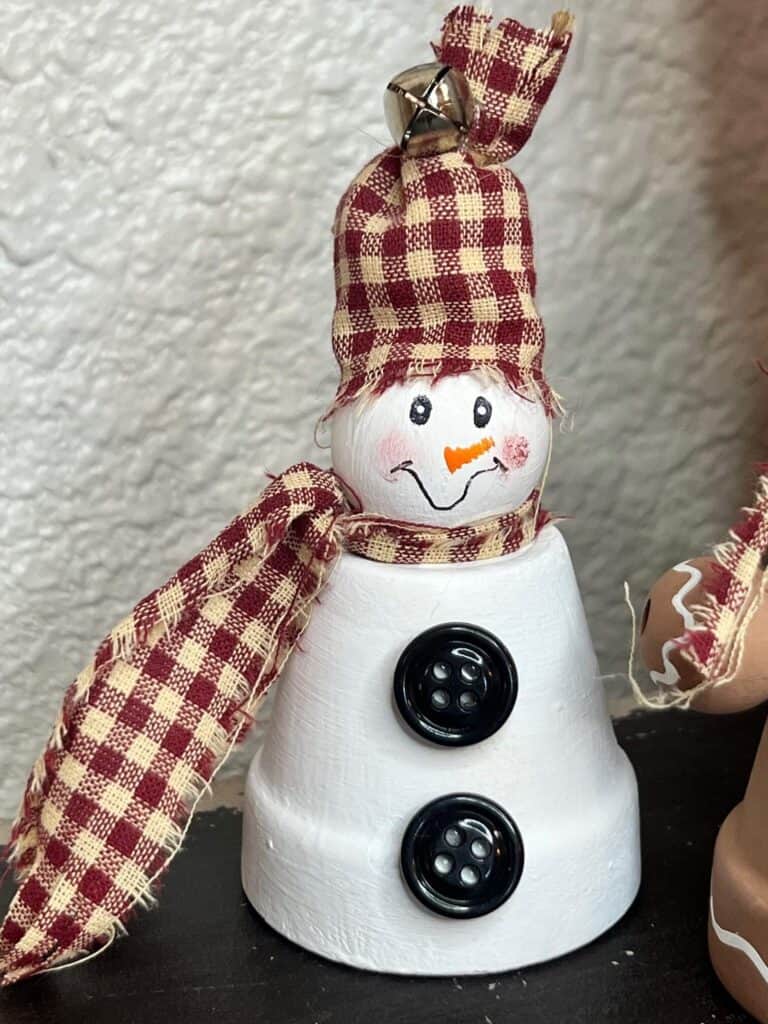 Mini terra cotta pot snowman with a wood bead head, black buttons, red homespun fabric scarf and hat and a simple hand painted face.