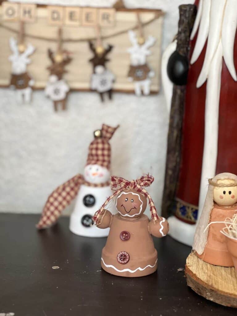 Mini terra cotta pot gingerbread man painted brown with a re homespun fabric bow on top of its bead head, red buttons and a simple hand painted face.