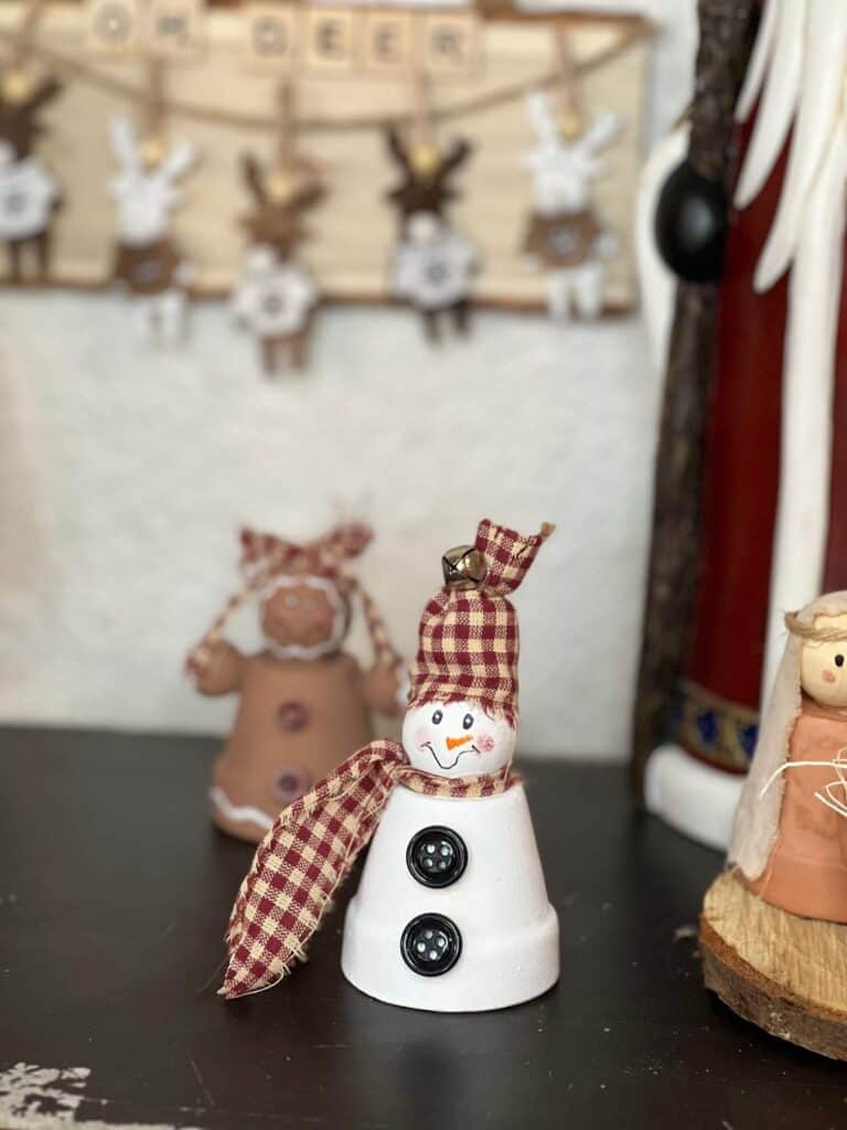 Mini terra cotta pot snowman with a wood bead head, black buttons, red homespun fabric scarf and hat and a simple hand painted face.