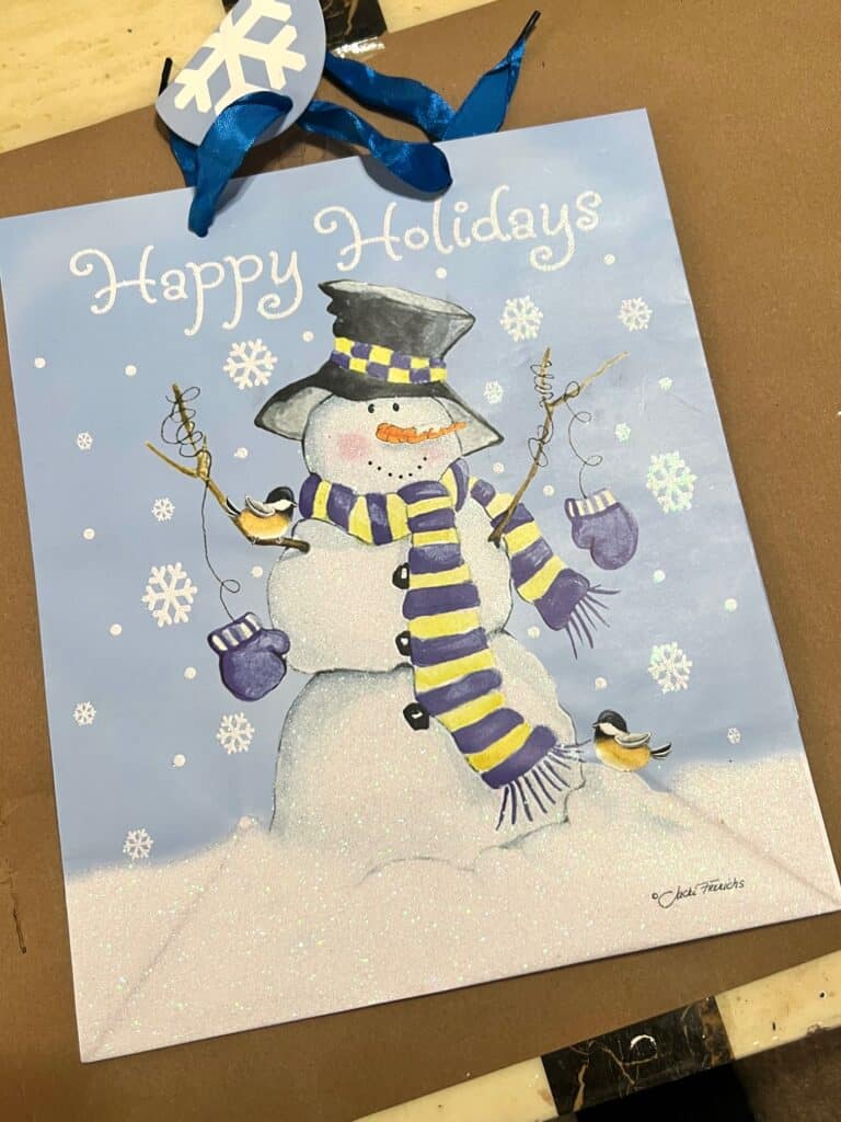 Blue Snowman Gift bag with a yellow and blue scarf that says "Happy Holidays" at the top.