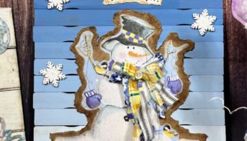Ombre Snowman Gift Bag Decor with blue to white ombre paint stick background, a winter snowman gift bag with snowflakes around the snowman and a white sign at the top that says "Brrr" for winter decor.