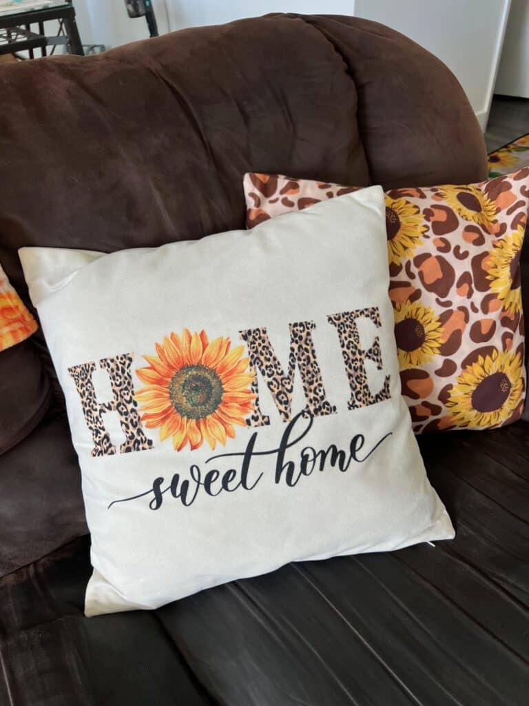 A throw pillow that says HOME sweet home with leopard print letters and the O is a sunflower, next to a leopard print and sunflower pillow on the couch.