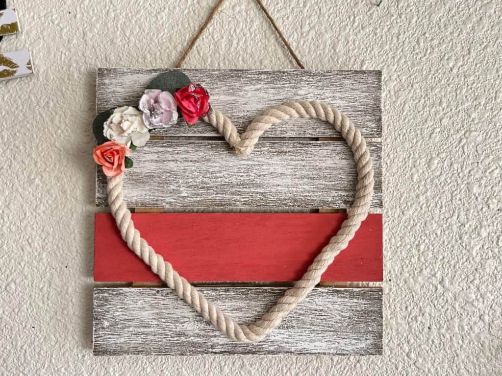 Wood Slatted background painted white and coral with a dollar tree nautical rope heart with pink, purple, and white faux flowers, for DIY valentines Day and everyday Home decor.