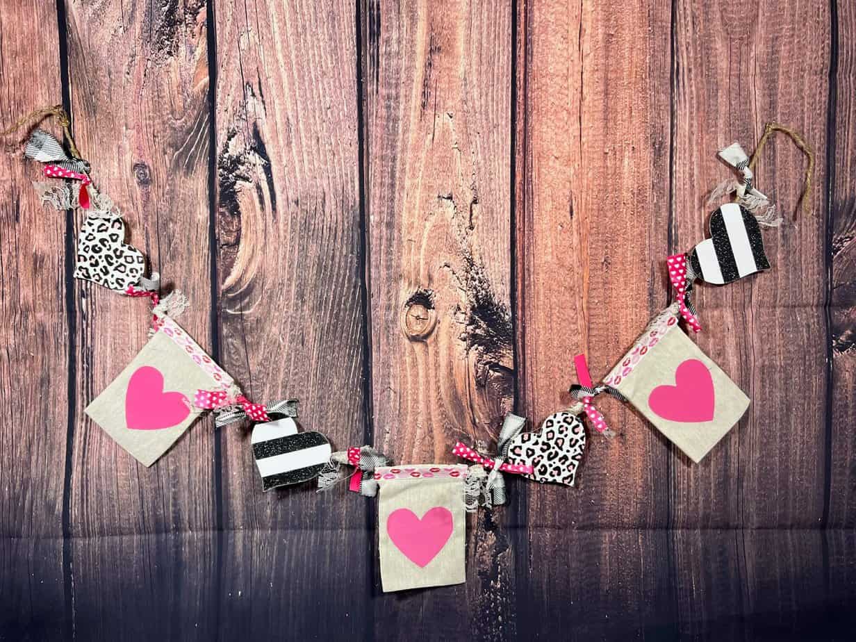 Dollar Tree Pink Heart Valentines Day Treat Bag banner with wood hearts with black and white stripes and pink leopard print, and fabric strips in between with pink and red lips. DIY Decor hanging garland for a Mantle or bookcase.