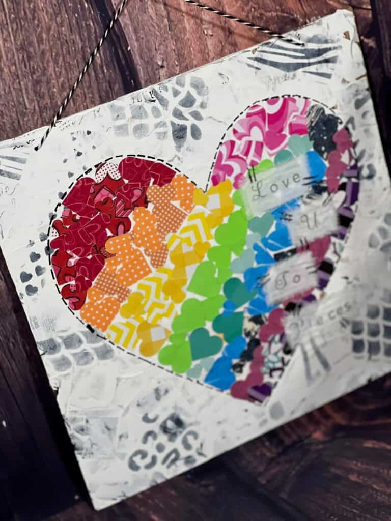 Rainbow Mixed Media Heart with a black and white background with animal print stencils, with a big heart in the middle that is made up of several smaller scrapbook paper hearts, that are rainbow color striped from left to right. DIY Valentines Day Home decor and crafts.