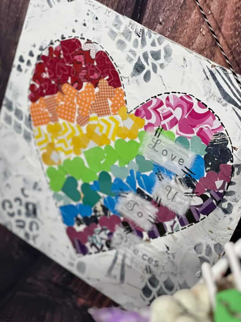 Rainbow Mixed Media Heart with a black and white background with animal print stencils, with a big heart in the middle that is made up of several smaller scrapbook paper hearts, that are rainbow color striped from left to right. DIY Valentines Day Home decor and crafts.
