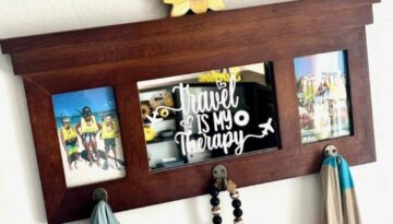 A thrift store coat rack mirror with the words "Travel is my Therapy" etched into it and a family vacation photo on each side of the mirror. The coat rack has a scarf and jacket hanging and a sunflower on top.