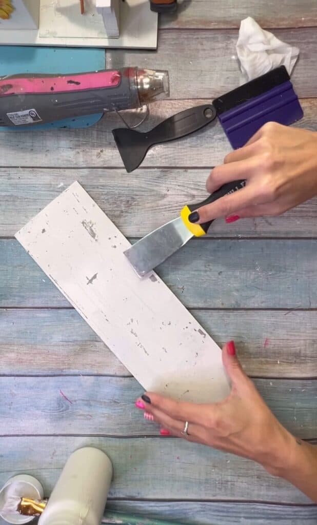A paint scraper being used to chip off the white paint on the background.