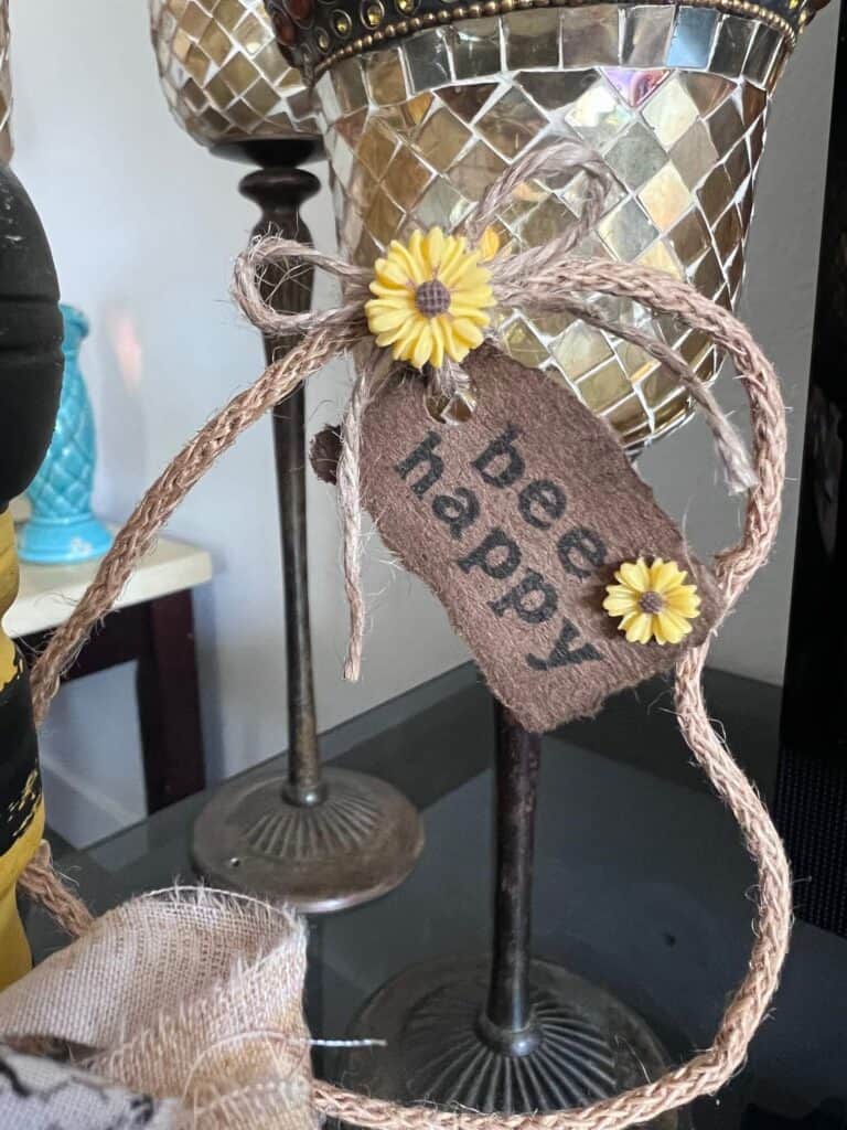 The wing made from wired jute with a small tag that says "Bee Happy" with small sunflower embellishments and a shoestring twine bow.