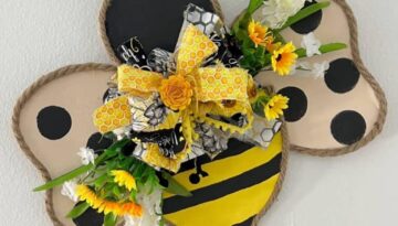 Cardboard Copycat Bumblebee Door Hanger with jute rope around the edge of the cardboard body and a black and yellow stripes with wings with black polka dots and a big messy fabric bow with flowers in the center.