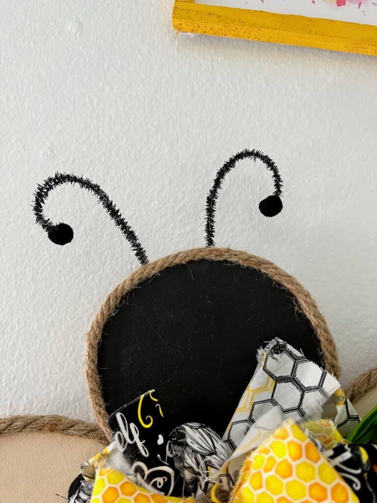 Closeup of the bees head showing antennas made with pipe cleaners and black craft pom poms.