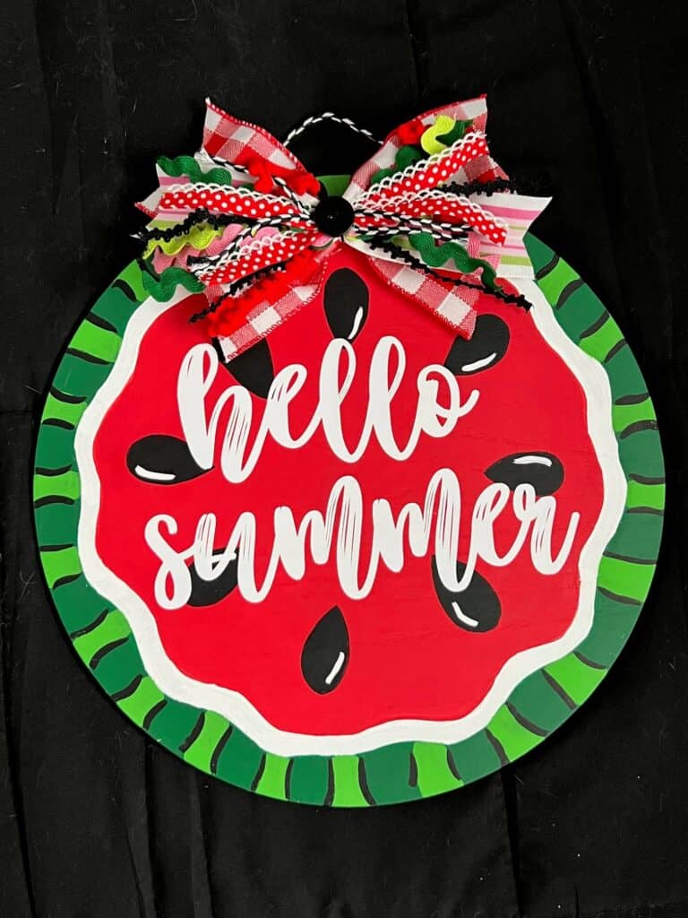 DIY Hello Summer Watermelon Door Hanger made with a wood round, a fabric bow, and white cricut vinyl to decorate your home front door.