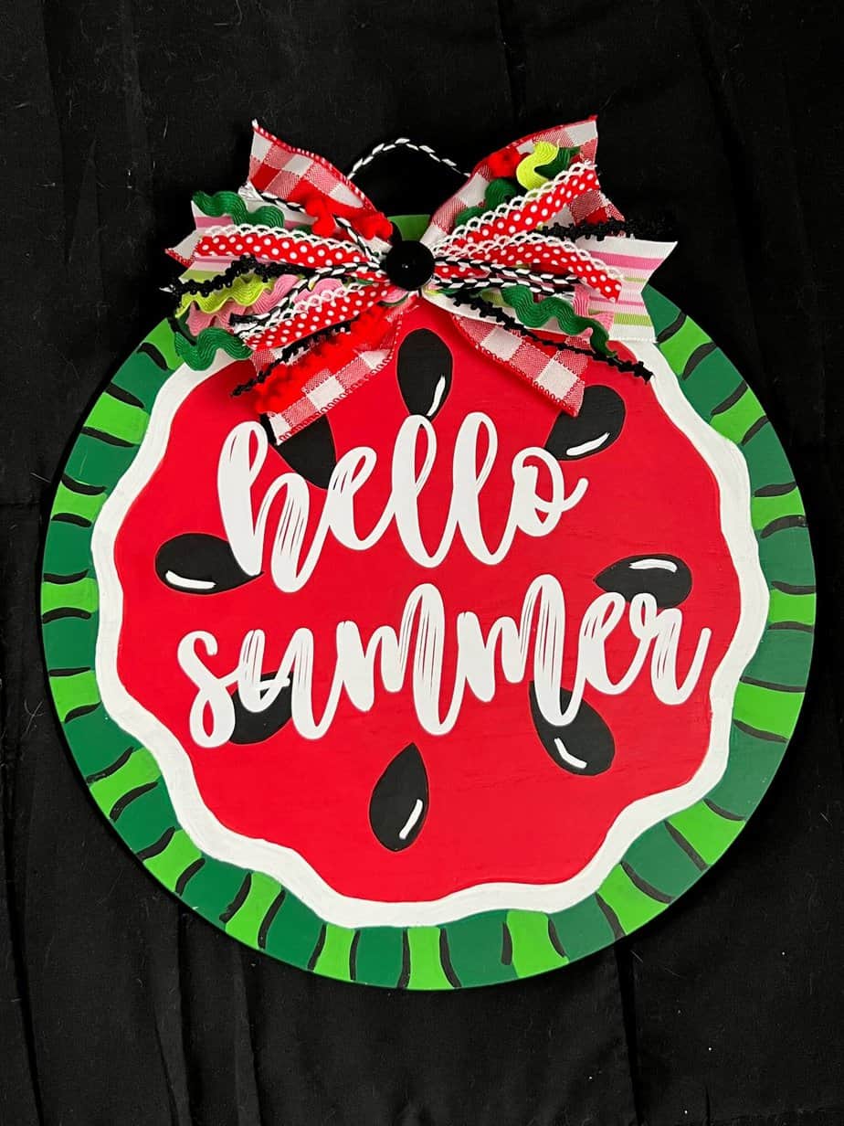 DIY Hello Summer Watermelon Door Hanger made with a wood round, a fabric bow, and white cricut vinyl to decorate your home front door.