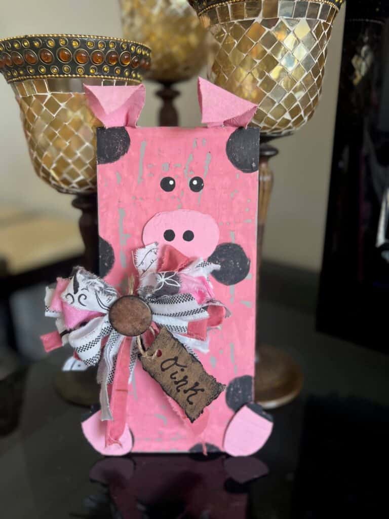 DIY affordable farmhouse wooden pig decor with chippy pink paint and black polka dots and a big messy fabric bow with a tag that says "oink oink"