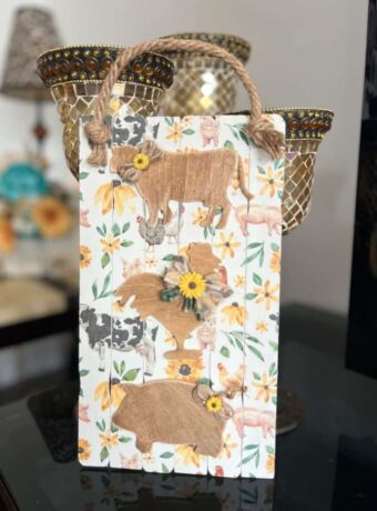 Wood Farm Animal DIY Decor Sign with a Pig, Cow, Rooster on a paint stick background with a decoupaged napkin that has farm animals and sunflowers. A jute rope hanger.