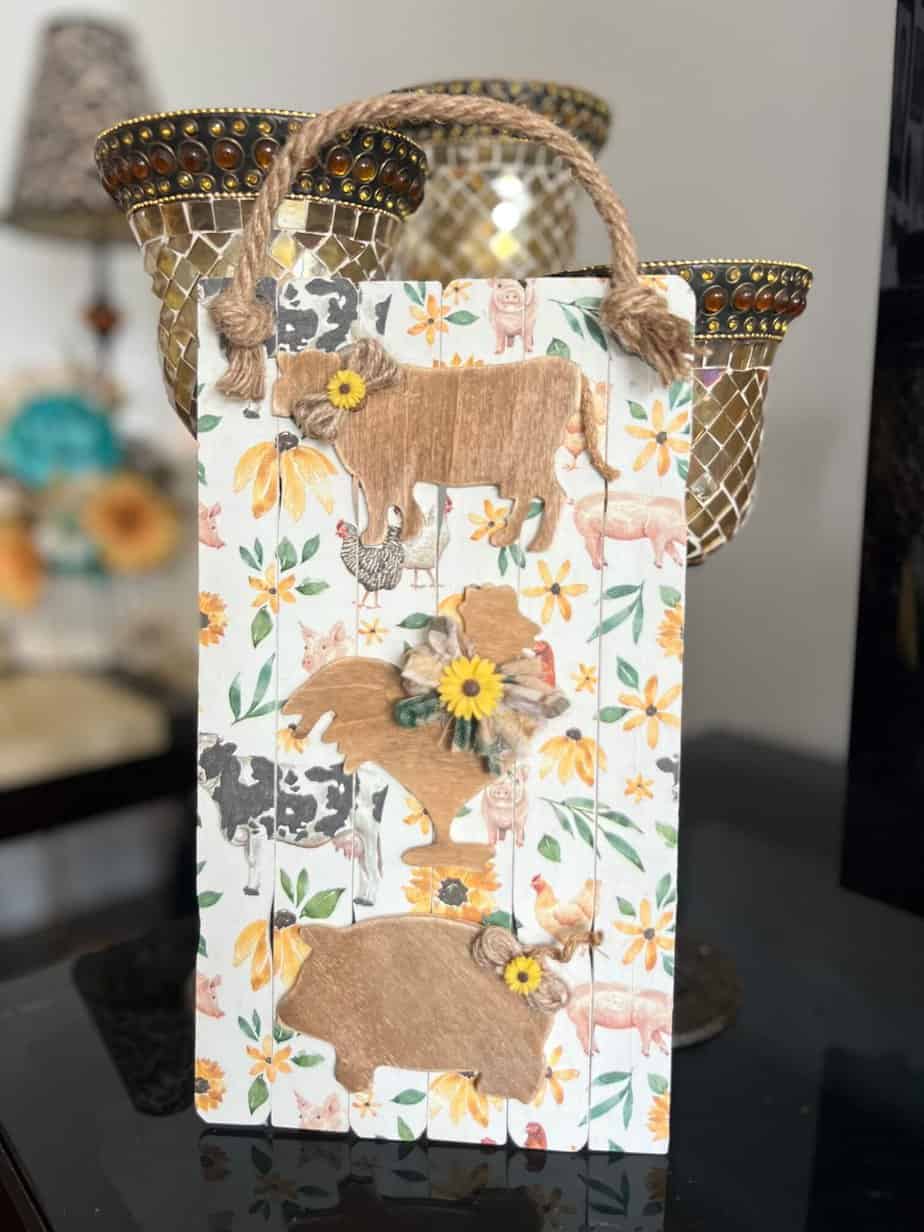 Wood Farm Animal DIY Decor Sign with a Pig, Cow, Rooster on a paint stick background with a decoupaged napkin that has farm animals and sunflowers. A jute rope hanger.