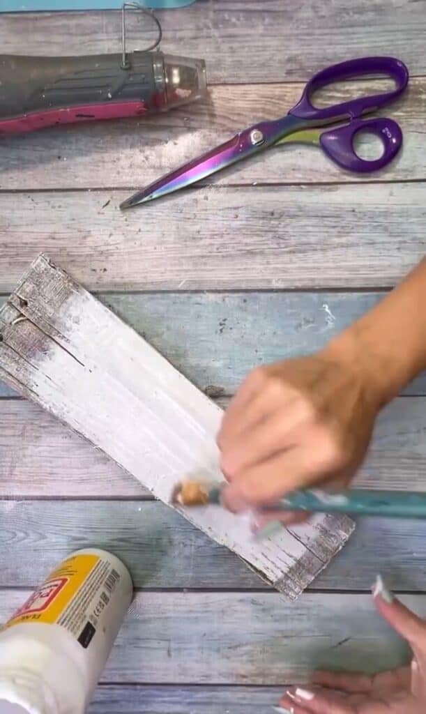 painting Mod Podge onto the scrap wood with a paint brush.