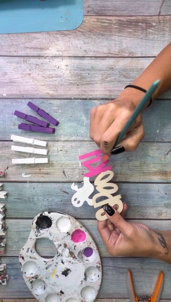 Painting the Dollar Tree ghost and spooky wood cutout pink to glue to the center of the Halloween Clothespin wreath.