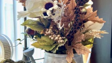 Thrifted watering can flipped into a galvanized metal watering can with a fall floral arrangement, leopard print and gold pumpkin picks, leopard print leaves, and gold acorns, with a leopard print and sunflower pumpkin napkin decoupaged to the front of the watering can for DIY fall centerpiece or home decor.