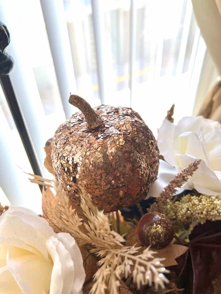 A sparkly gold pumpkin pick sticking out of the fall floral arrangement.