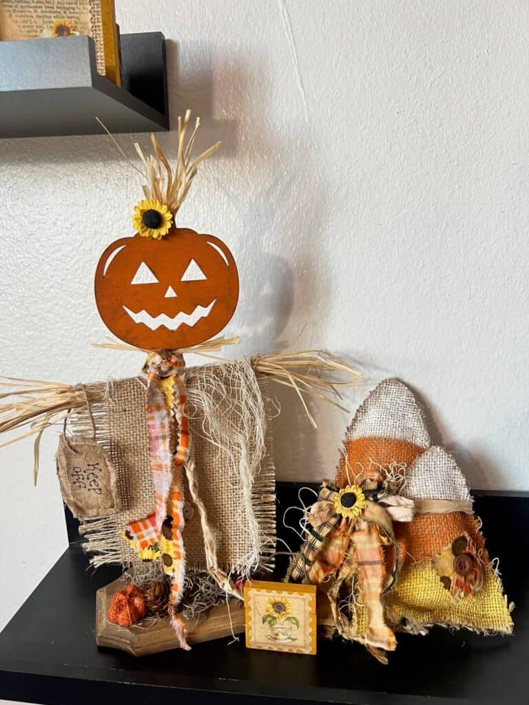 A pumpkin head scarecrow on a shelf with the completed candy corn craft.