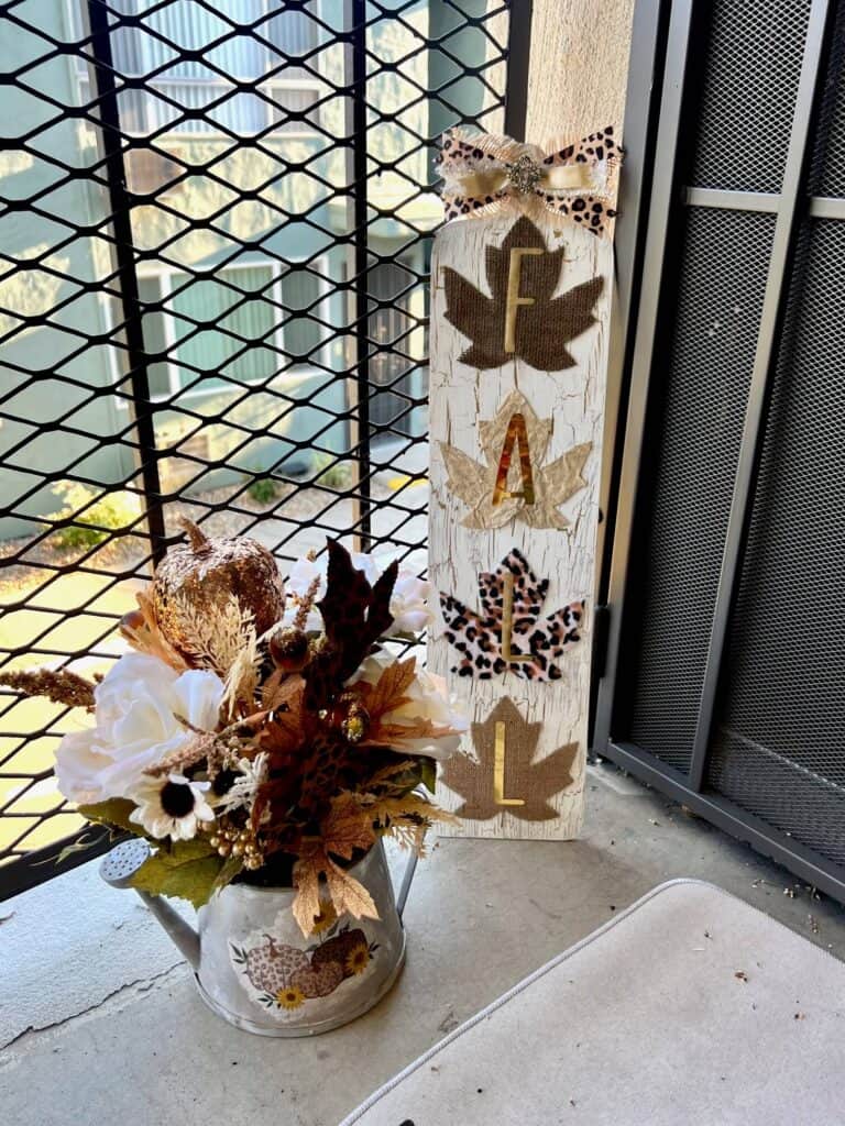 The completed thrifted fall floral watering can next to a FALL porch sign that coordinates with eachother.