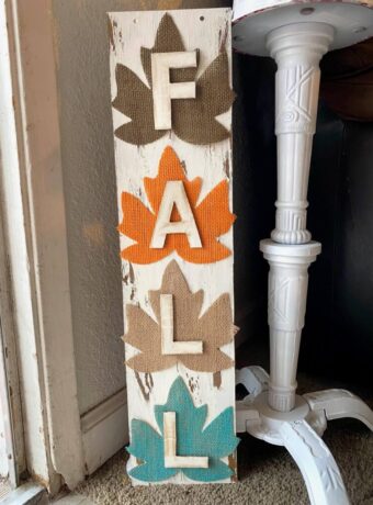 DIY Dollar tree long sign with 4 burlap fall leaves, one brown, orange, tan, and teal, that says FALL. The sign has a white chippy background perfect for decorating your home this autumn season.