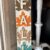 DIY Dollar tree long sign with 4 burlap fall leaves, one brown, orange, tan, and teal, that says FALL. The sign has a white chippy background perfect for decorating your home this autumn season.