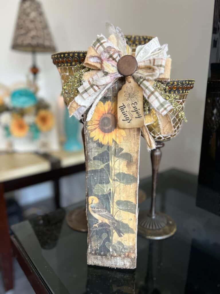 DIY Scrap wood sunflower decor with a free sunflower printable on rice paper, decoupaged onto a piece of scrap wood and a big messy fabric bow with a hangtag that says "enjoy the little things".